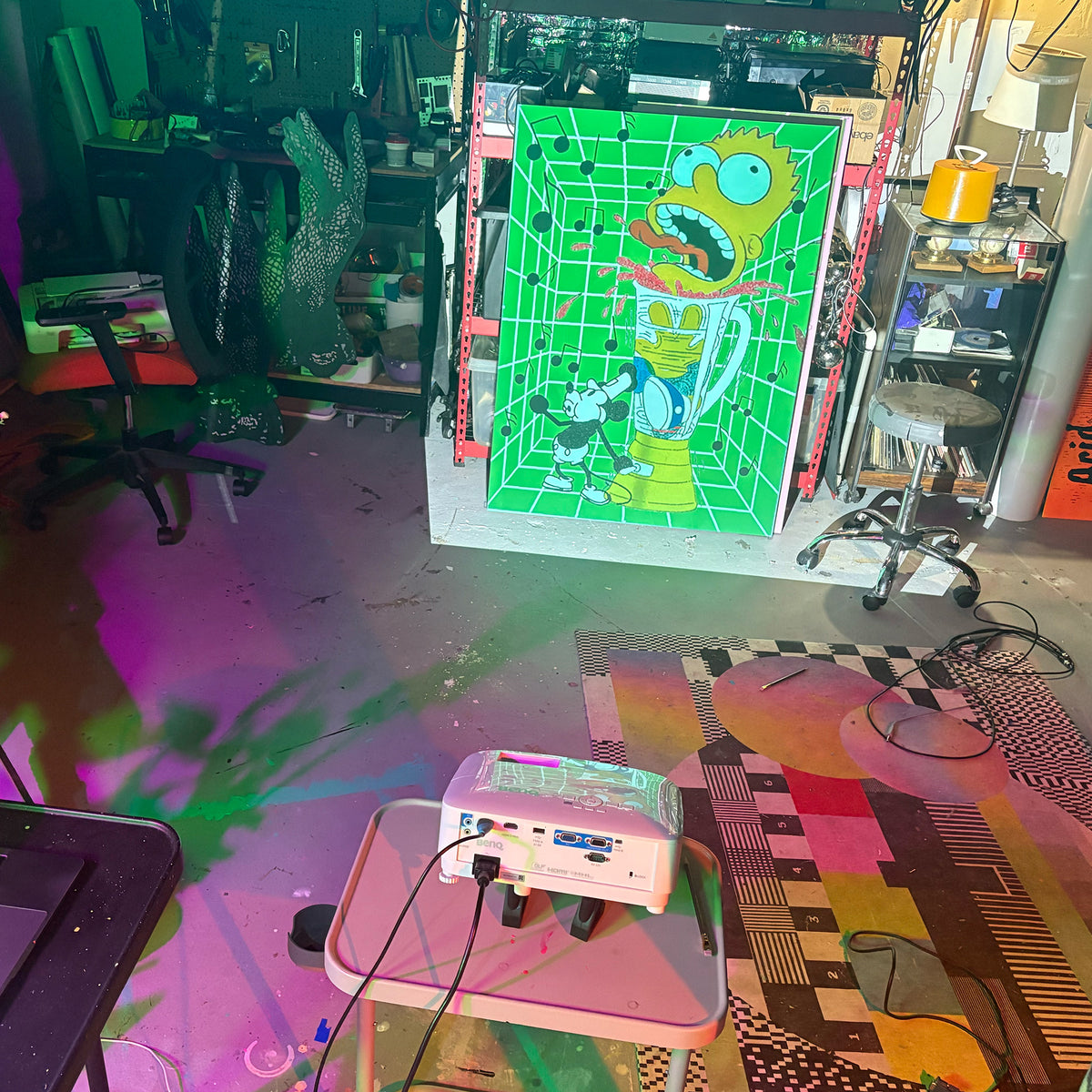 A large projected art featuring a green grid background and bart simpson in a blender being murdered by mickey mouse, displayed in a cluttered studio or workshop with a projector on a table in the foreground by Palm Treat