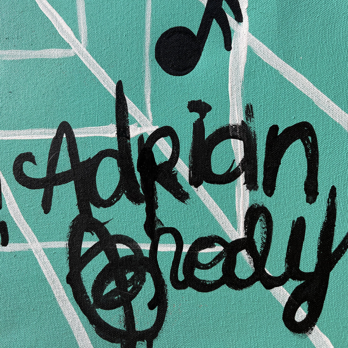 Close-up of a painted canvas featuring the name 'Adrian Brody' in bold black brushstrokes over a teal background with white intersecting lines and a black musical note by Palm Treat.