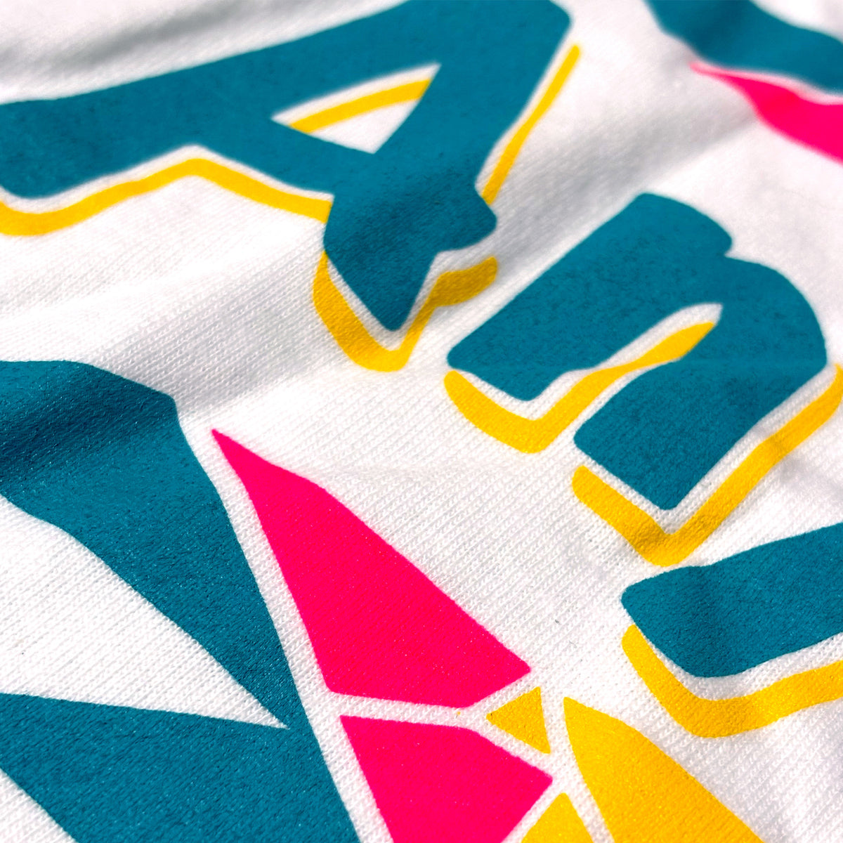 Close-up of a white fabric surface with large colorful graphic lettering in teal, yellow, and hot pink.
